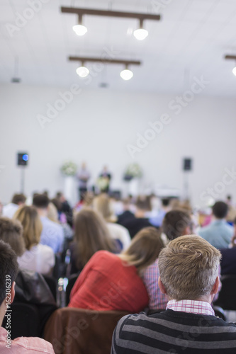 Business Ideas. Group of People Sitting in hall During a Conference. Two Male Hosts Speaking on Stage in Front of the Audience. © danmorgan12
