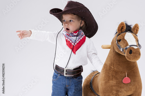 Little Children Consepts. Caucasian Girl in Cowgirl Clothing Posing With Symbolic Plush Horse Against White. Directing Forward. photo
