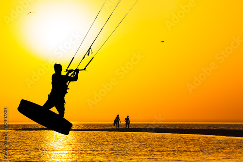 Silhouette of kitesurfer over the sea on sunset background