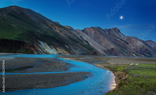 Night view to colorful mountain ridge and river flowing down in valley with sheep eating grass, Landmannalaugar, Iceland
