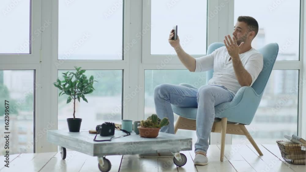 Young happy man have online video chat using digital tablet computer sitting on balcony in modern loft apartment Young happy man have online video chat using digital tablet computer sitting on balcony in modern loft apartment