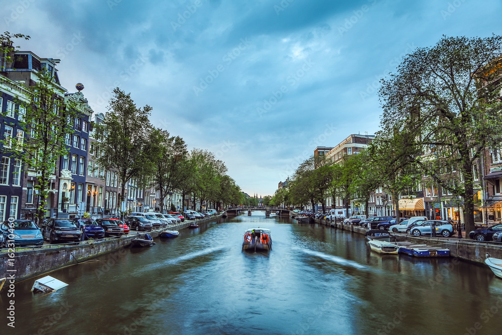 The most famous canals and embankments of Amsterdam city during sunset. General view of the cityscape and traditional Netherlands architecture.