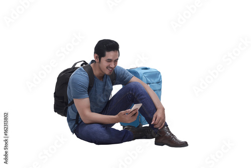 Portrait of a young man sitting with suitcase and sending text message