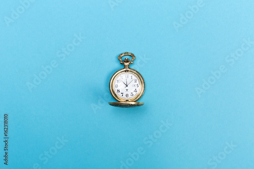 Small golden watch on a light blue background