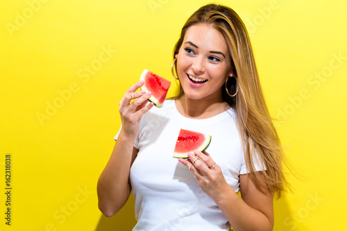 Happy young woman holding watermelons on a yellow background