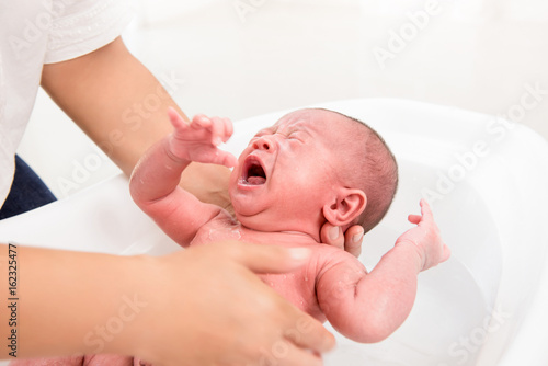 Little newborn baby crying while being taken a bath