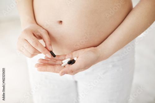 Close up of pregnant woman holding prescription pills suffering from nausea or allergy. Healthy pregnancy concept. High key.