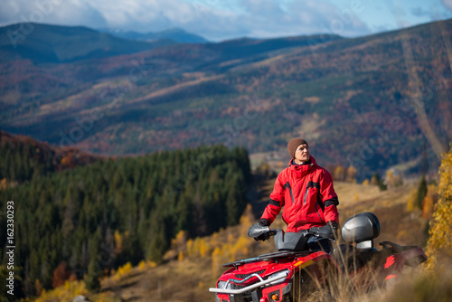 Guy riding on quad bike in the mountains on a blurred background mighty mountains and forests in the autumn sunny day