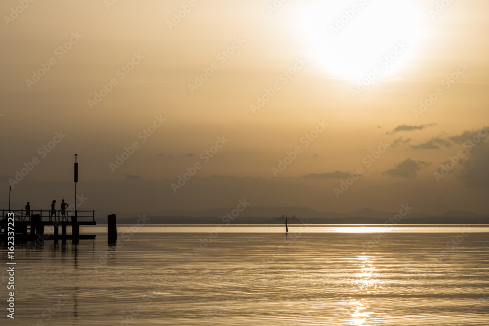 A lake at almost sunset, with beautiful and surreal golden colors, and some people silhouettes on a pier