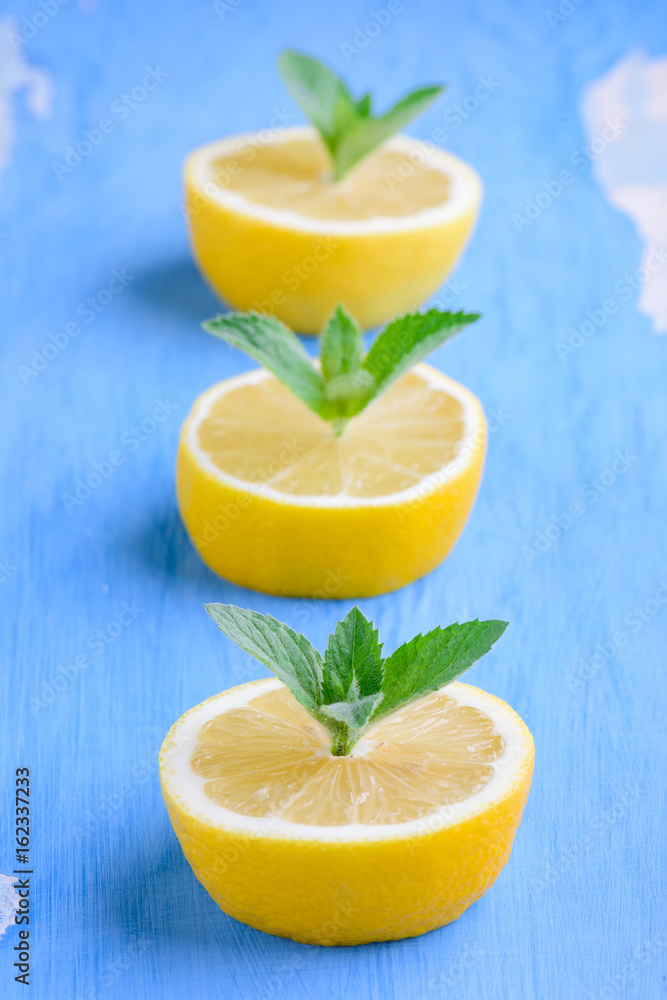 Cut the lemons with sprigs of mint on a blue background. The lemon and mint on old painted surface blue color Cut the lemons with sprigs of mint on a blue background. The lemon and mint on old painted surface blue color
