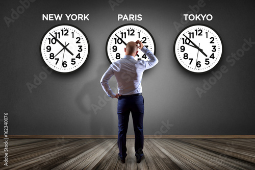 Businessman in front of a wallwith clocks of different country - Jetlag concept photo
