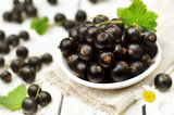 Sweet fresh ripe blackcurrants in plate with daisies on wooden background, selective focus