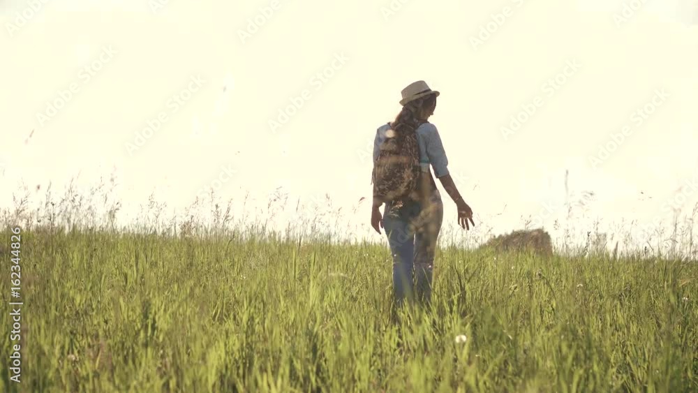 young girl hipster in the hat is on the field. woman traveler with a backpack seen from behind young girl hipster in the hat is on the field. woman traveler with a backpack seen from behind
