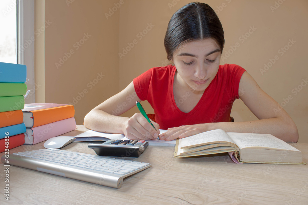 Smiling teenager girl doing homework at the table at home.Girl student with pile of books and notes studying indoors Smiling teenager girl doing homework at the table at home.Girl student with pile of books and notes studying indoors