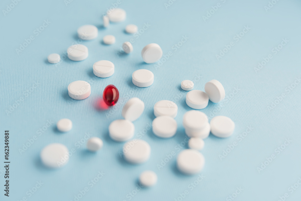 Close up of white tablets with one red capsule Close up of white tablets with one red capsule