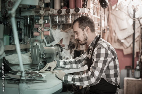 male worker sewing stitches on belt in leather workshop