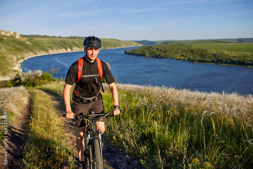 Attractive cyclist riding the mountain bike on the summer trail above the river. Attractive cyclist riding the mountain bike on the summer trail above the river.