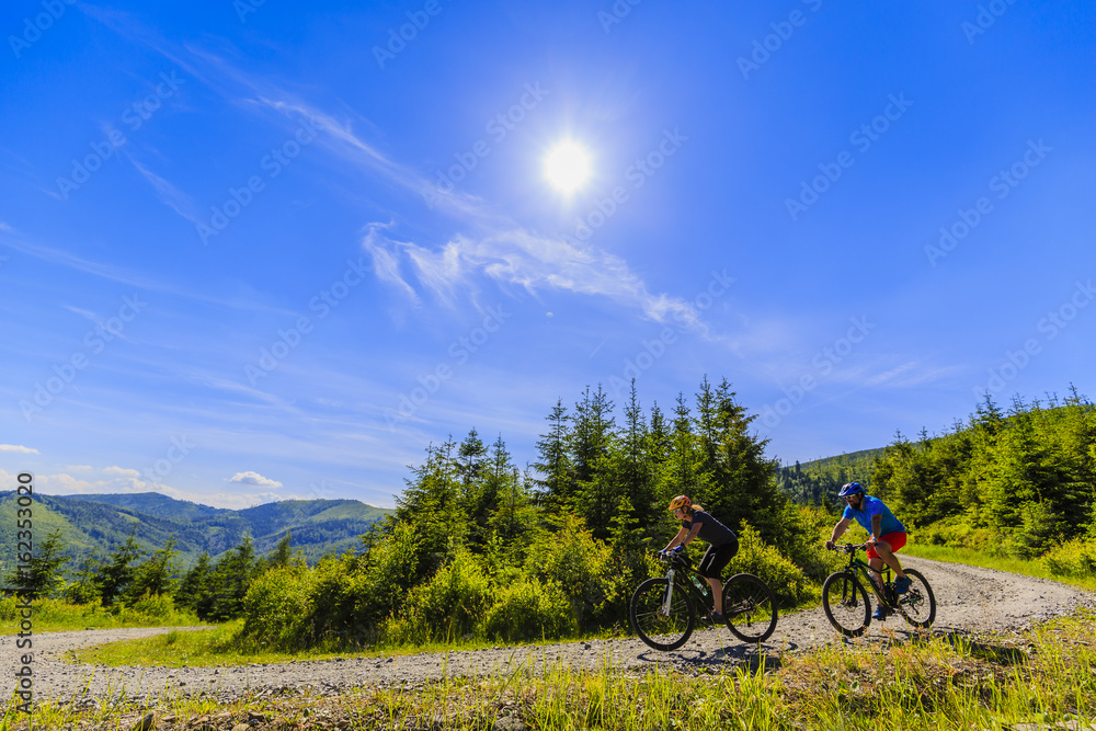 Mountain biking women and man riding on bikes in early spring mountains forest landscape. Couple cycling outdoor sport activity. Mountain biking women and man riding on bikes in early spring mountains forest landscape. Couple cycling outdoor sport activity.