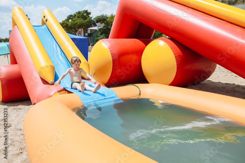 The boy is entertained outdoors, bathed in an inflatable pool. Slides down from the slide into the water.