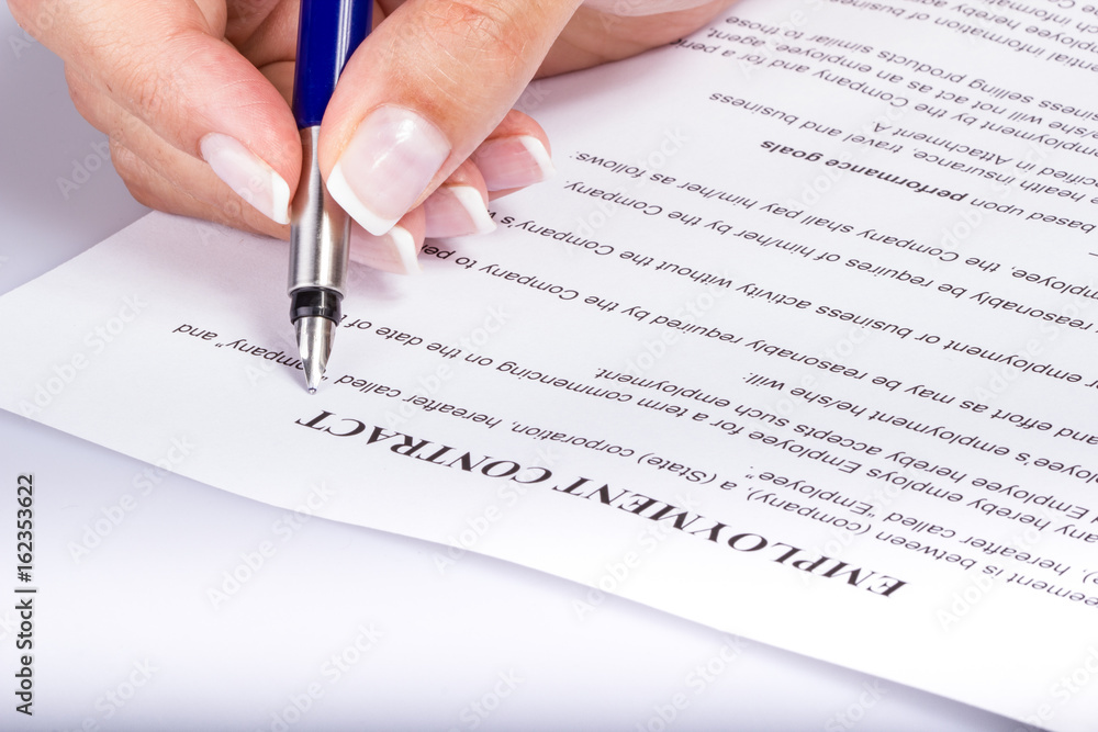 Employee signing the employment contract, closeup of a female hand holding a fountain pen above the legal document Employee signing the employment contract, closeup of a female hand holding a fountain pen above the legal document