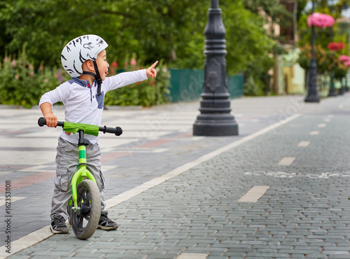 Fototapeta Naklejka Na Ścianę i Meble -  Child boy in white helmet riding on his first bike with a helmet. Bike without pedals.
