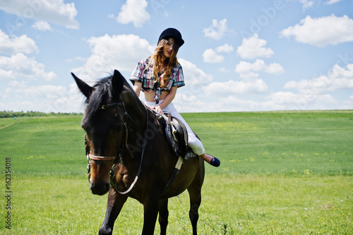 Young pretty girl riding a horse on a field at sunny day.