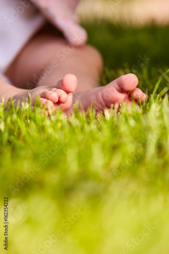 Baby feet in the green grass at summer warm day in the city park.