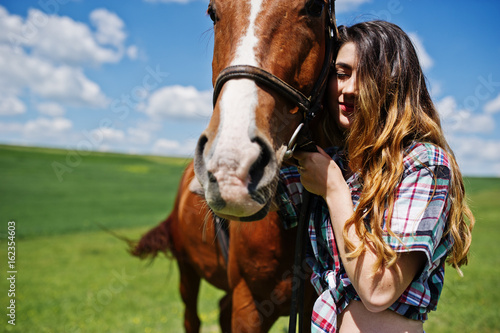 Young pretty girl stay with horse on a field at sunny day.