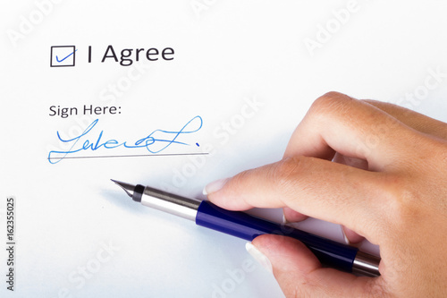 Agreement signature closeup, female hand holding a blue fountain pen checked the "I Agree" checkbox