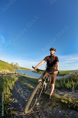 Attractive cyclist standing with bike and observing the view against blue sky.