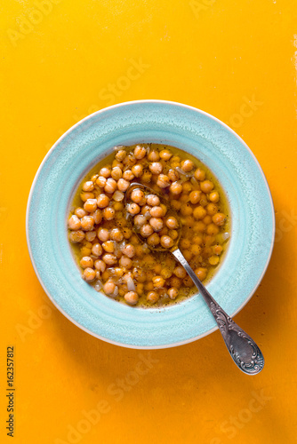 Greek chickpea soup in the white plate on the yellow background  vertical photo