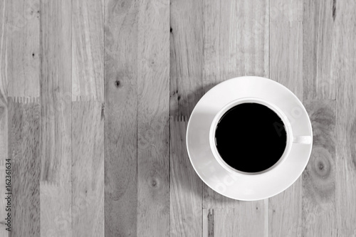 Coffee cup with black coffee on wood table, top view with copy space, monochrome effect