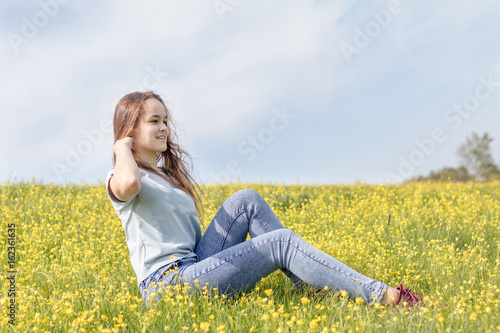 Young girl teenager on a lawn field with yellow flowers. Long chestnut hair. Sunshine, springtime, blue sky. Coloring and processing photos with soft selective focus. Shallow depth of field.
