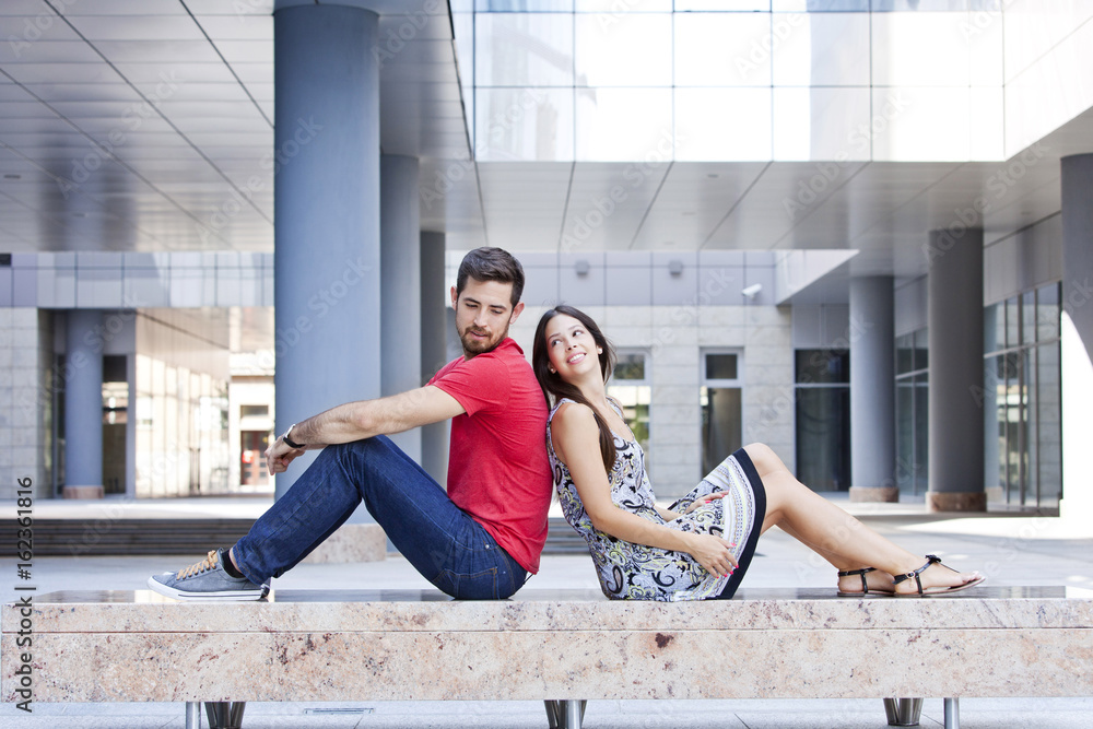 Happy young couple sits back to back on campus Happy young couple sits back to back on campus