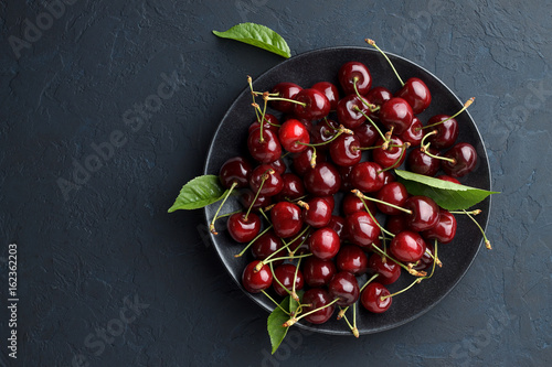 Ripe sweet cherry in black plate on dark stone background.
