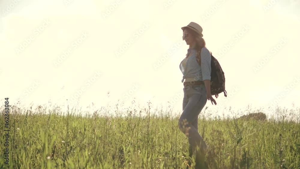 young girl tourist goes on a meadow. woman traveler wearing sunglasses, a hat and a backpack young girl tourist goes on a meadow. woman traveler wearing sunglasses, a hat and a backpack