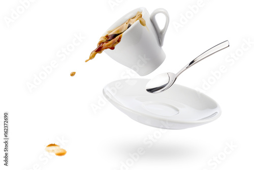 cup of coffee spils with saucer and spoon and coffee falls on white background