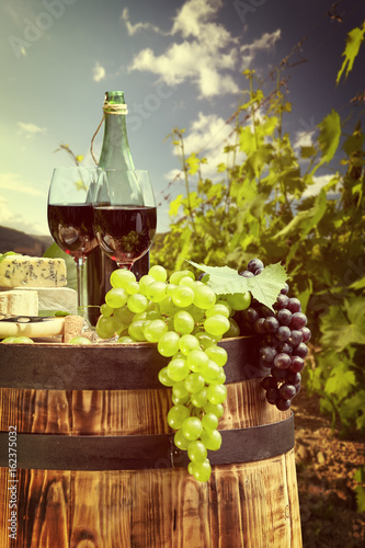 Fototapeta Naklejka Na Ścianę i Meble -  Red wine bottle and wine glass on wodden barrel. Beautiful Tuscany background