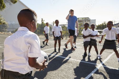 Fototapet Teacher plays football with young kids in school playground