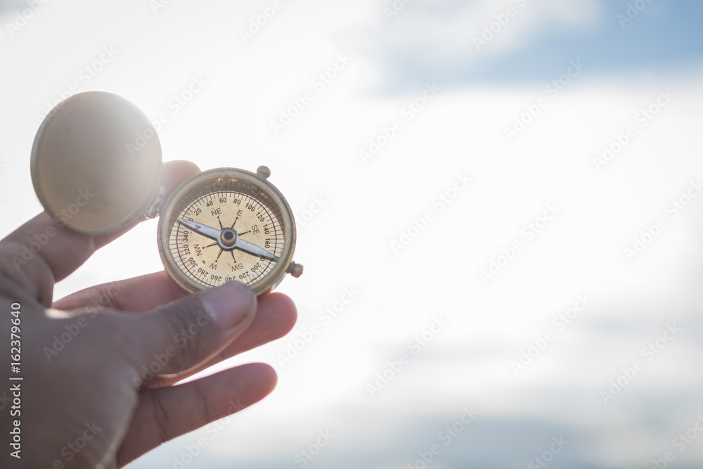 Fototapeta premium Hand with compass at mountain road at sunset sky 