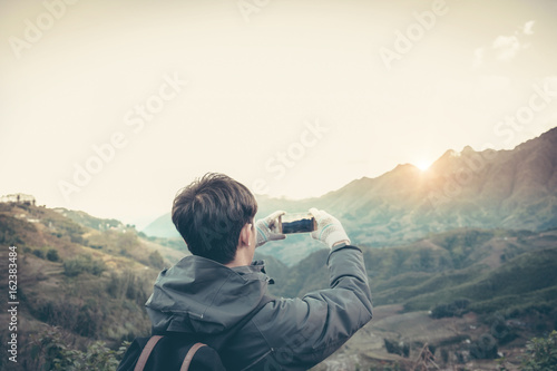 traveler photographing mountain and sun and sky by smartphone.