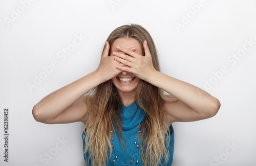 Headshot of young adorable blonde woman with cute smile on white background covers her face with palms