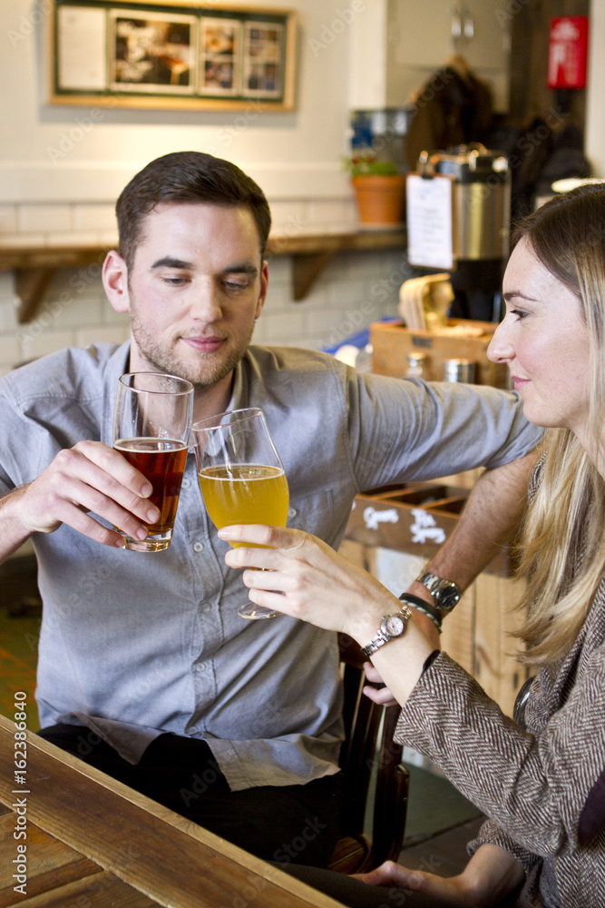 Young couple toasting with beer in pub, Dorset, Bournemouth, England Young couple toasting with beer in pub, Dorset, Bournemouth, England