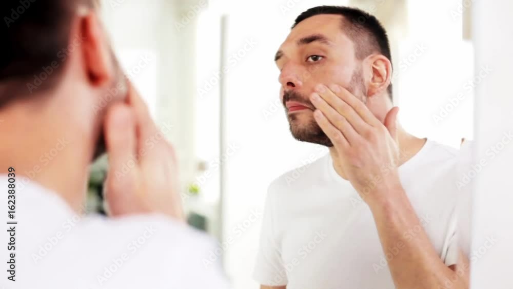 happy young man applying cream to face at bathroom happy young man applying cream to face at bathroom