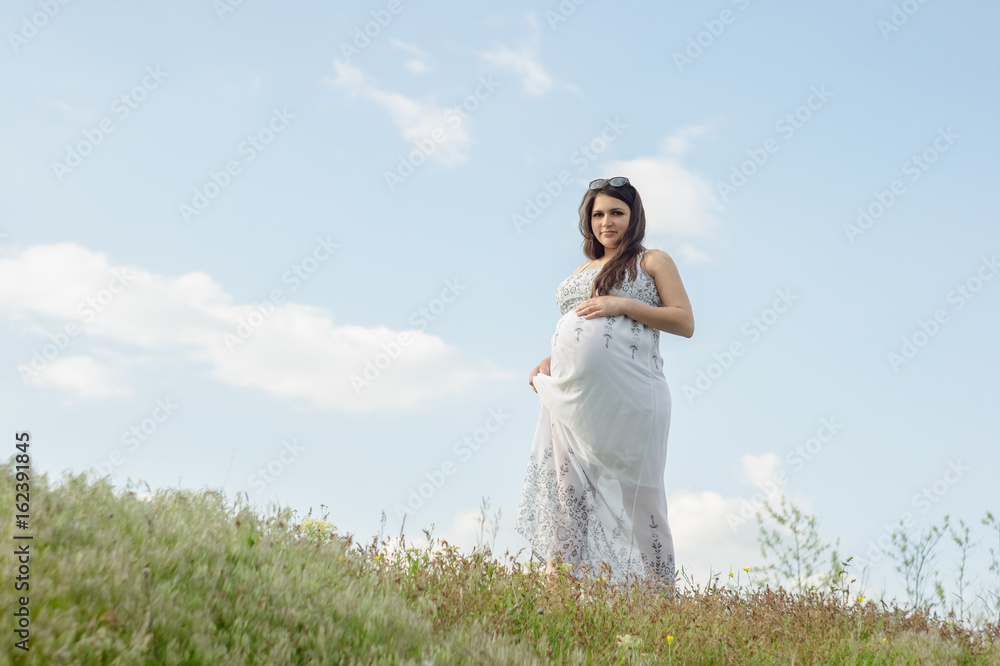 Pregnant woman in white dress, resting on a flowering meadow in summer Pregnant woman in white dress, resting on a flowering meadow in summer
