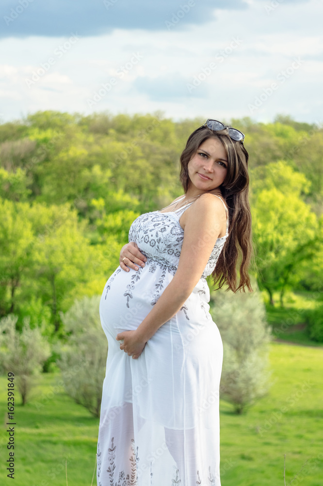 Pregnant woman in white dress, resting on a flowering meadow in summer Pregnant woman in white dress, resting on a flowering meadow in summer