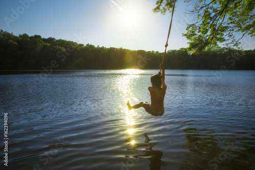 boy bungee jumping over water. kid swings on a rope and ready to jump into the water. Back view. The concept of healthy lifestyle