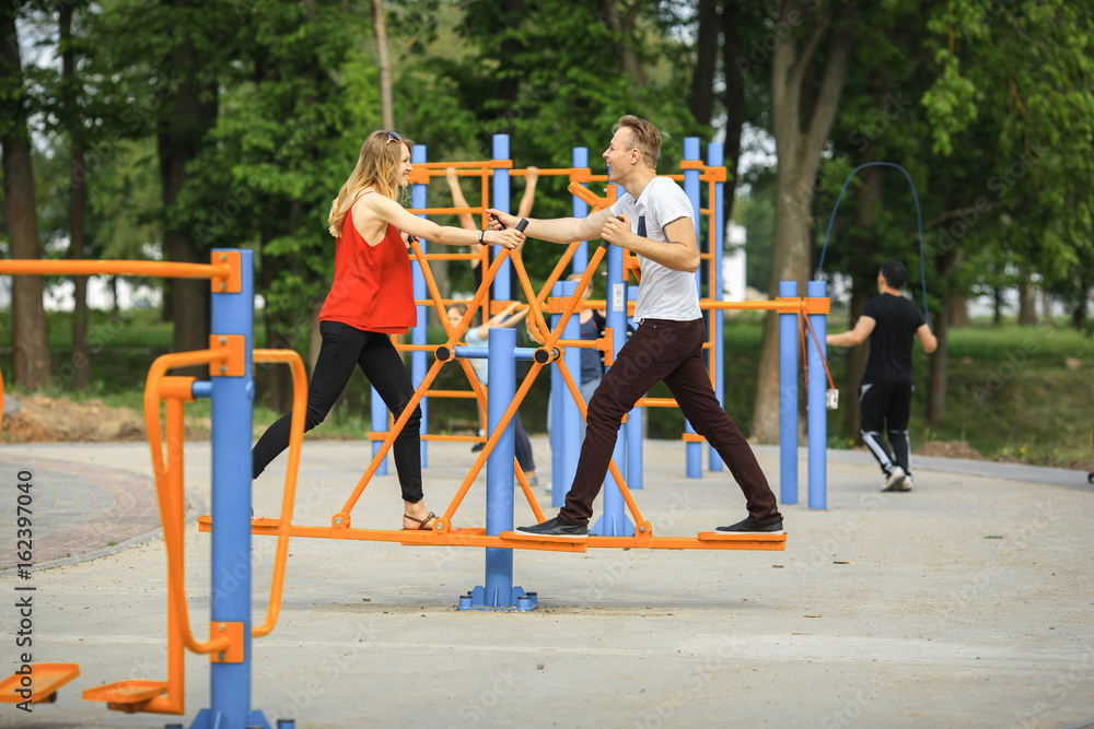 Fototapeta premium Street workout and love. A loving couple is engaged in fitness on a sports ground on a sunny summer day. Young boy and girl.
