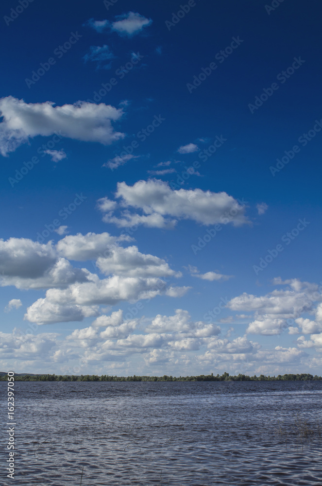 Summer river under a high blue sky with white clouds.