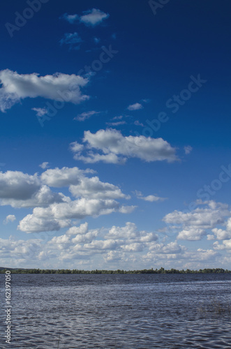 Summer river under a high blue sky with white clouds.